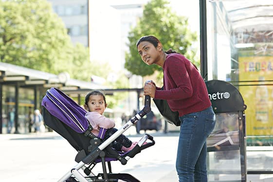 Mamma utomhus skjuter ett mindre barn i en sittvagn. 