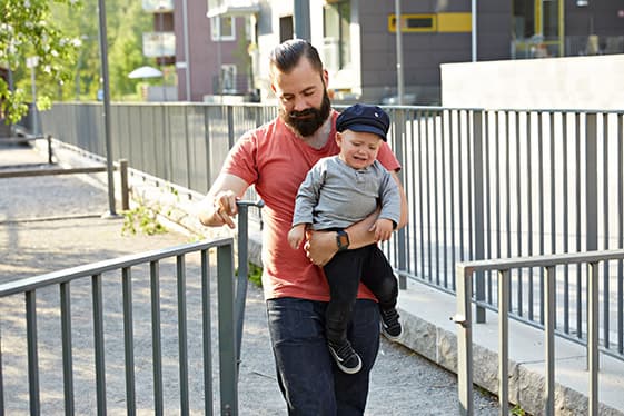 Pappa går genom en grind med gråtande mindre barn i famnen. 